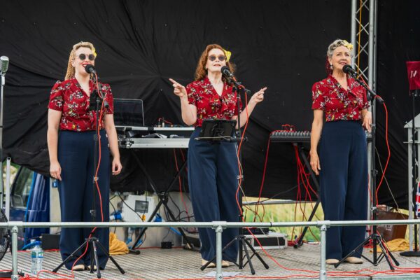 Three female singers on stage, wearing matching outfits and performing for a 1940s weekend event