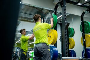 Leisure attendant in lime green t-shirt putting back weights onto a stack in a gym