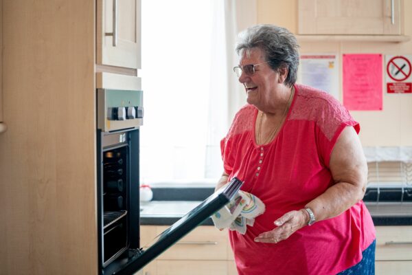 Lady wearing a red top opening an eye level oven door and looking inside.